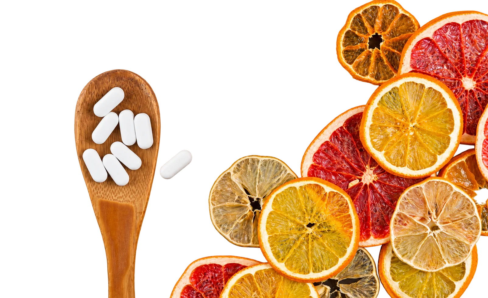 Une cuillère en bois remplie de comprimés blancs posée sur un fond noir, à côté de tranches séchées d'orange, de citron et de pamplemousse.