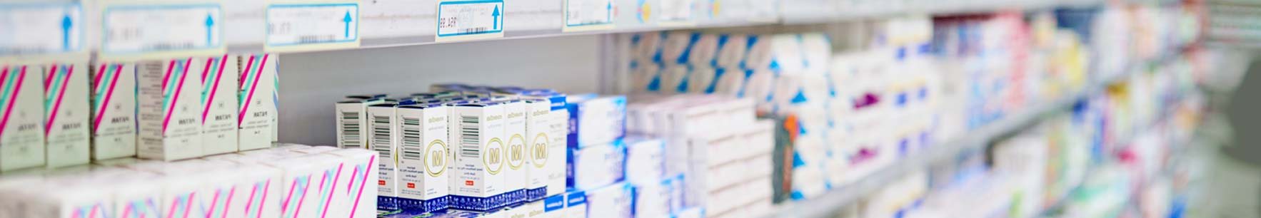 Rayons de pharmacie garnis de nombreuses boîtes de médicaments blanches, bleues et rayées de rose, avec des étiquettes de prix en haut.