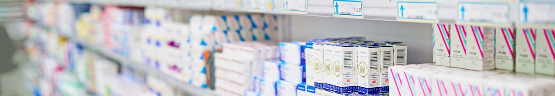 Vue panoramique de rayonnages de pharmacie garnis de nombreuses boîtes de médicaments blanches, bleues et roses avec des étiquettes de prix.